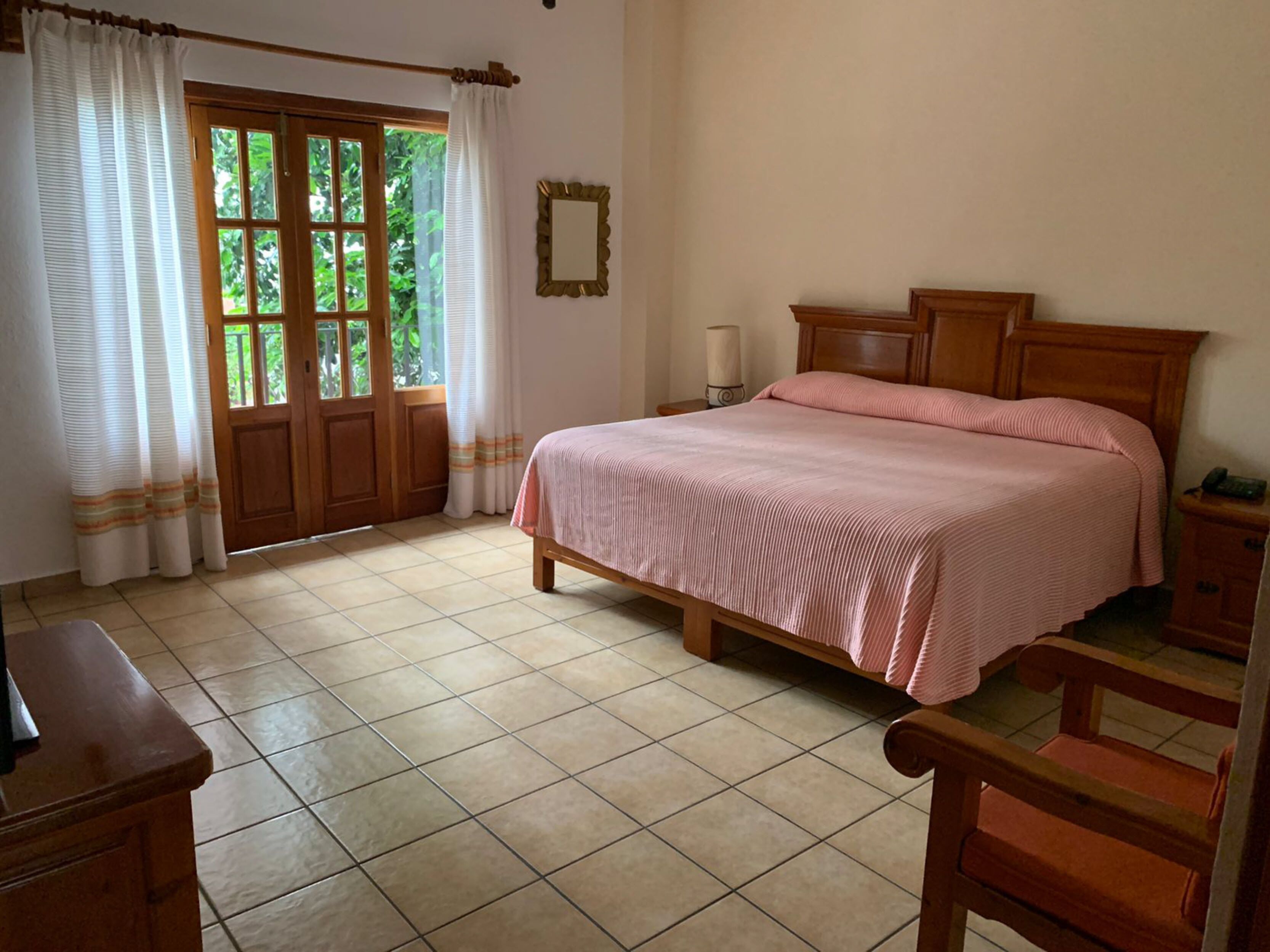 Un dormitorio con cama de madera, mesita de noche, silla, escritorio y ventana con cortinas.