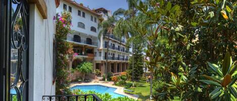 A resort with a swimming pool, lush greenery, and a multi-story building with balconies.