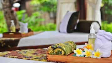 Un espacio de spa con una cama, una mesa de masajes, una botella de aceite, una toalla y flores.