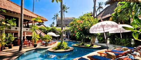 A pool area with lounge chairs, umbrellas, and tropical plants.