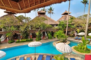 A pool area with lounge chairs and umbrellas, surrounded by thatched-roof buildings and palm trees. - Sativa Sanur Cottages (Denpasar)