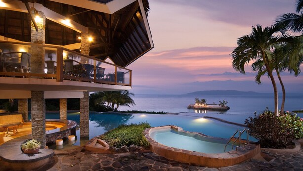 A resort with a pool, outdoor seating, and a view of the ocean at dusk. - Mithi Resort & Spa (Dauis)