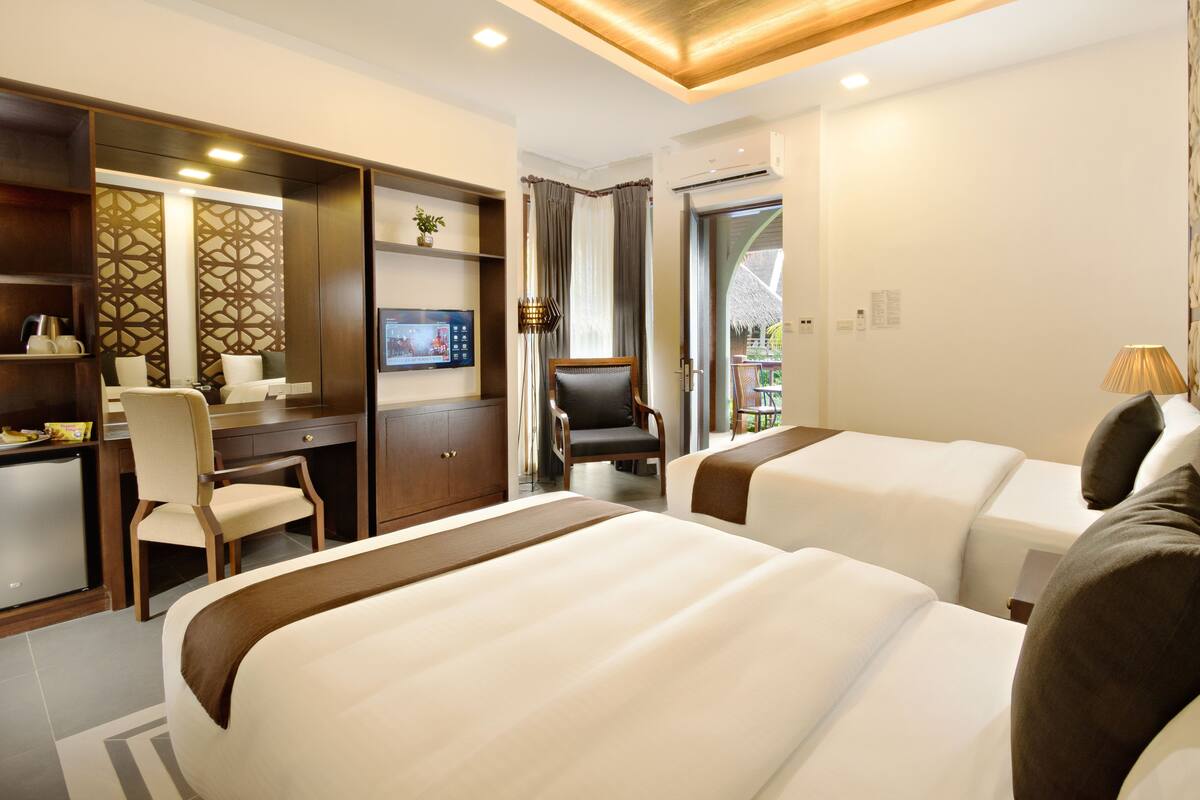 A hotel room with two beds, a desk with a chair, a television, and a view of the outdoors.