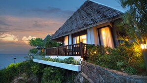 A beachfront villa with a thatched roof, a balcony with a wooden railing, and a view of the sea. - Mithi Resort & Spa (Dauis)