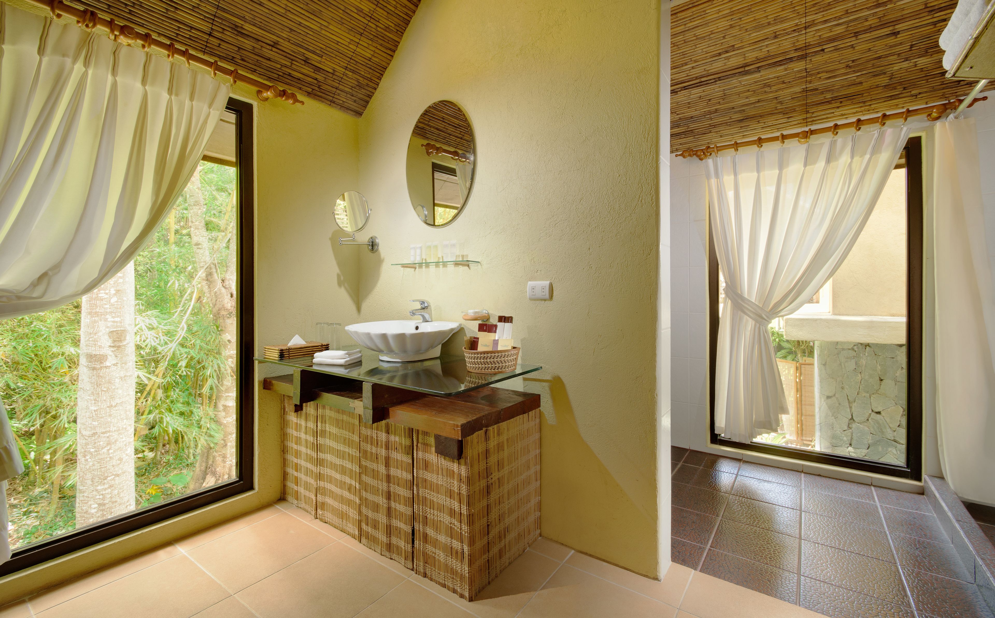 A bathroom with a large window, a sink, a mirror, and a shower area.