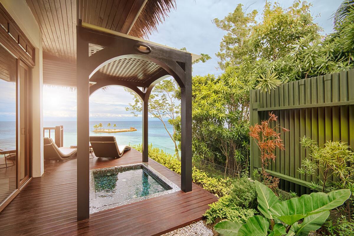 A wooden deck with a pool, lounge chairs, and a view of the ocean.