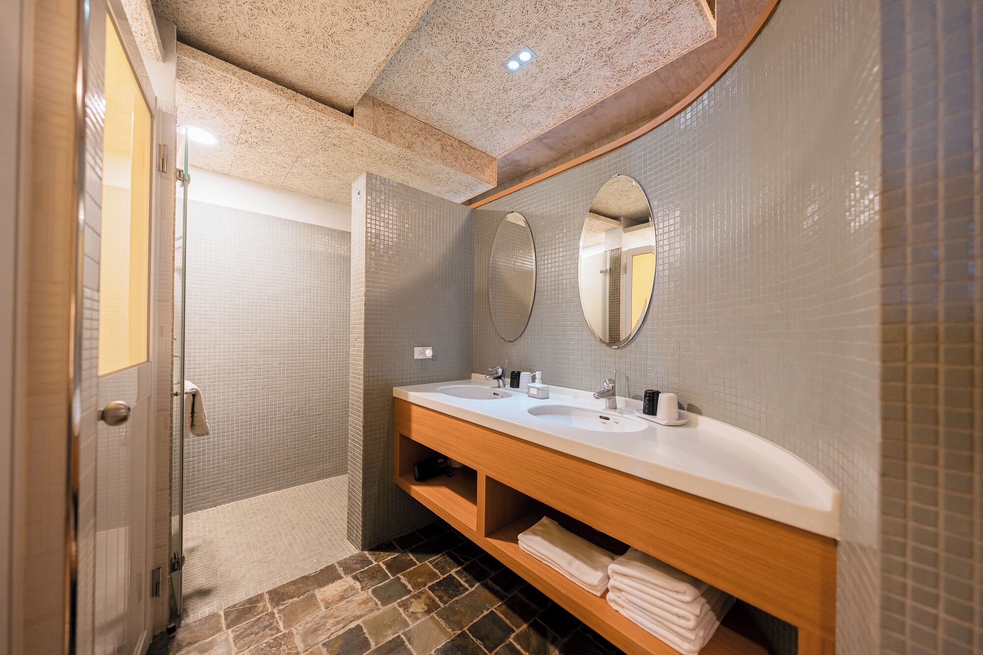 A bathroom with a shower, two sinks, and a wooden vanity.