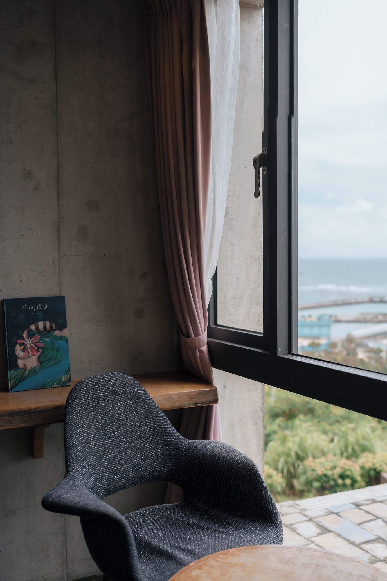 A room with a view of the sea, a chair, a table, and a book on the wall.