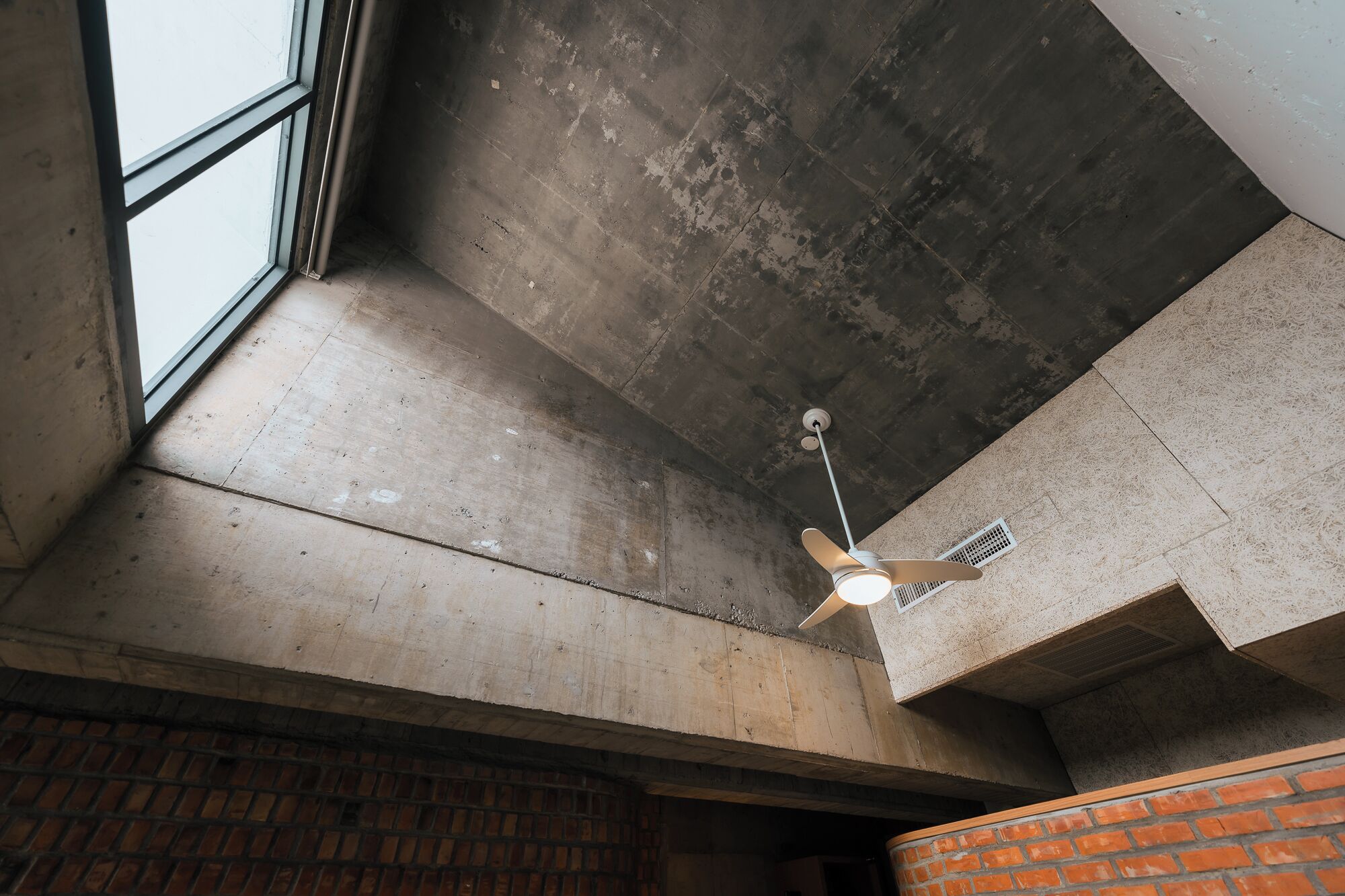 Ventilador de techo en una habitación con paredes de concreto y ladrillo a la vista.