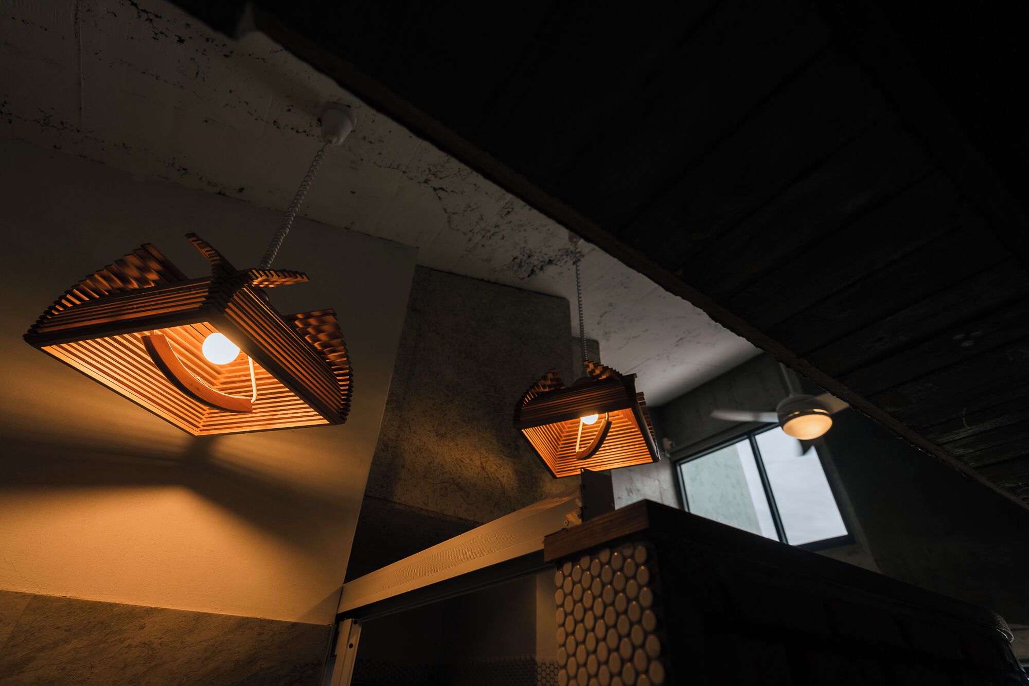 Dos lámparas colgantes de estilo farol en una habitación tenuemente iluminada, con techo de hormigón y una ventana al fondo.