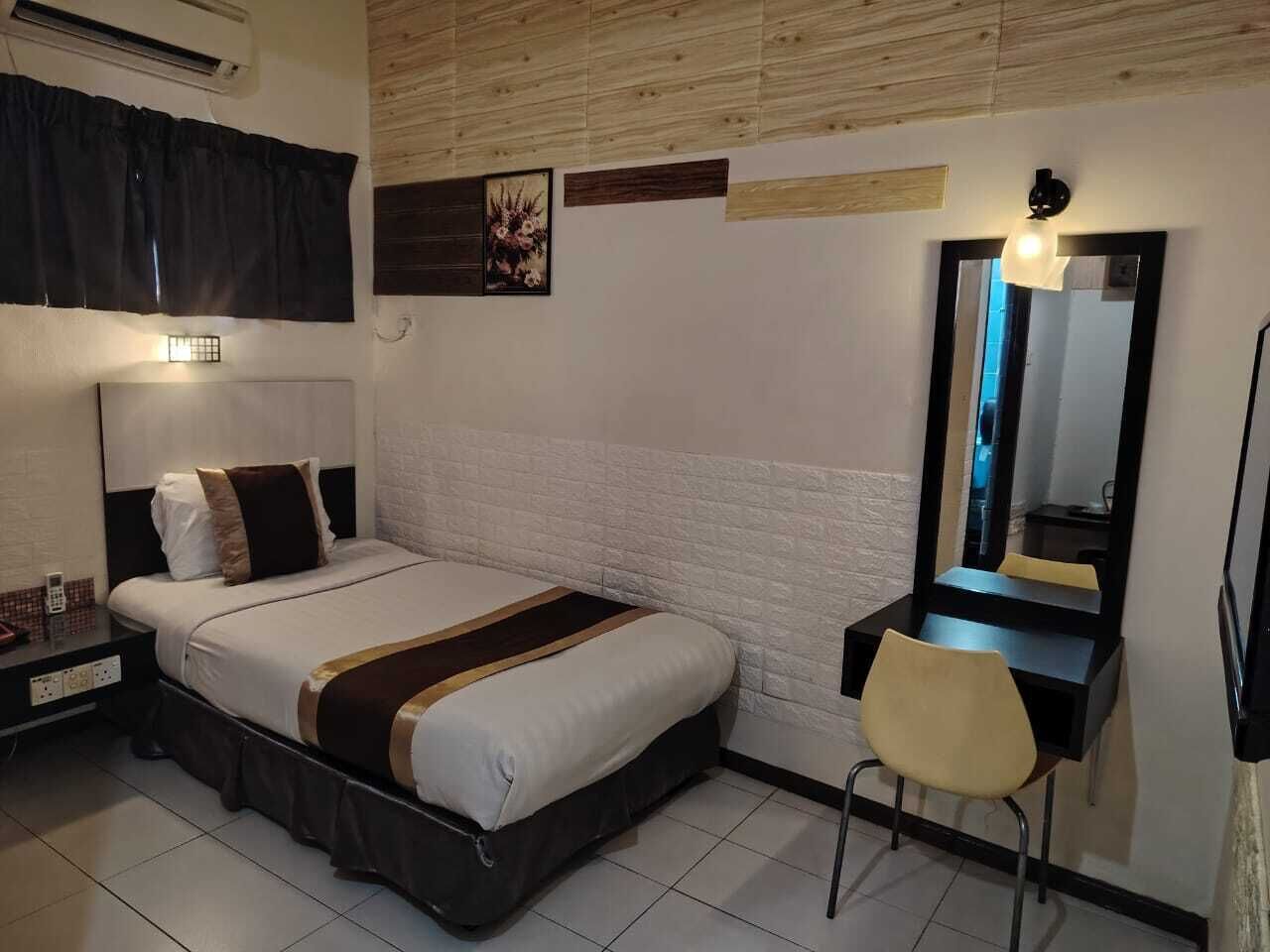 A hotel room with a bed, bedside table, chair, desk, mirror, and wall-mounted air conditioning unit.