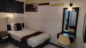Habitación de hotel con cama, mesita de noche, silla, escritorio, espejo y aire acondicionado instalado en la pared.