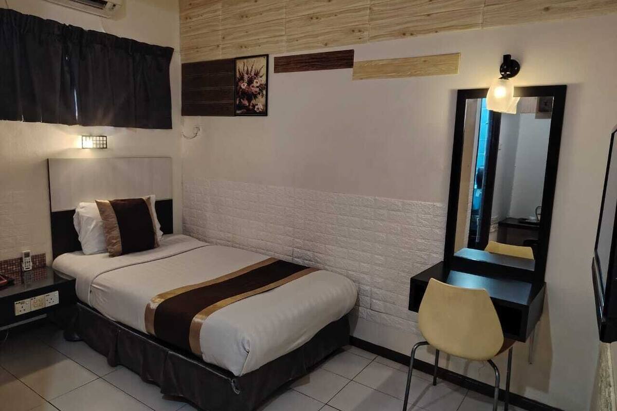 A hotel room with a bed, bedside table, chair, desk, mirror, and wall-mounted air conditioning unit.