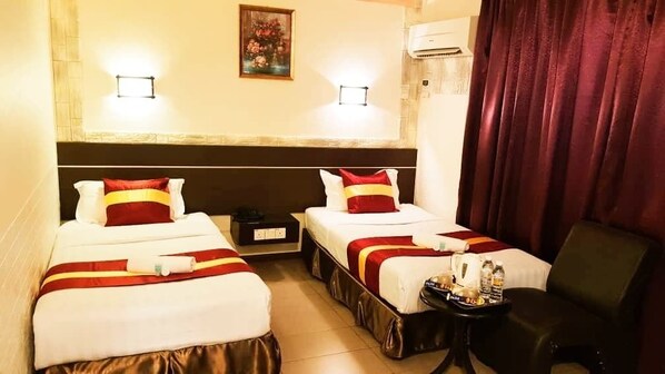 Quarto de hotel com duas camas, uma mesinha com produtos de higiene pessoal e uma cadeira.