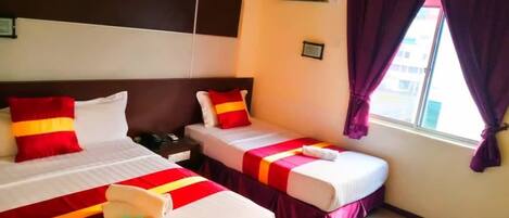 A hotel room with two beds, each with red and white bedding, a nightstand, an air conditioning unit, and a window with purple curtains.
