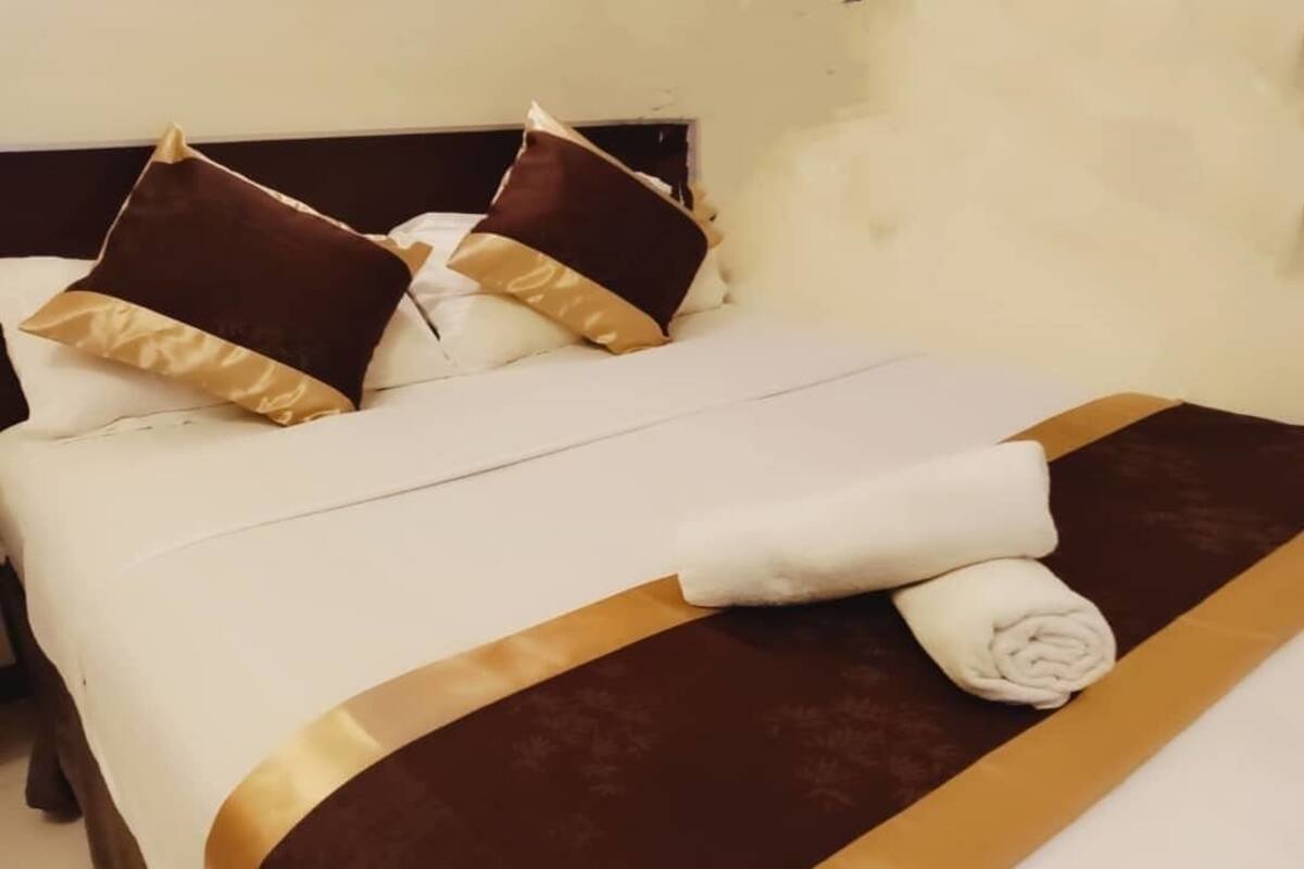 A neatly made bed with a white and brown bedspread, two brown pillows, and a folded white towel.