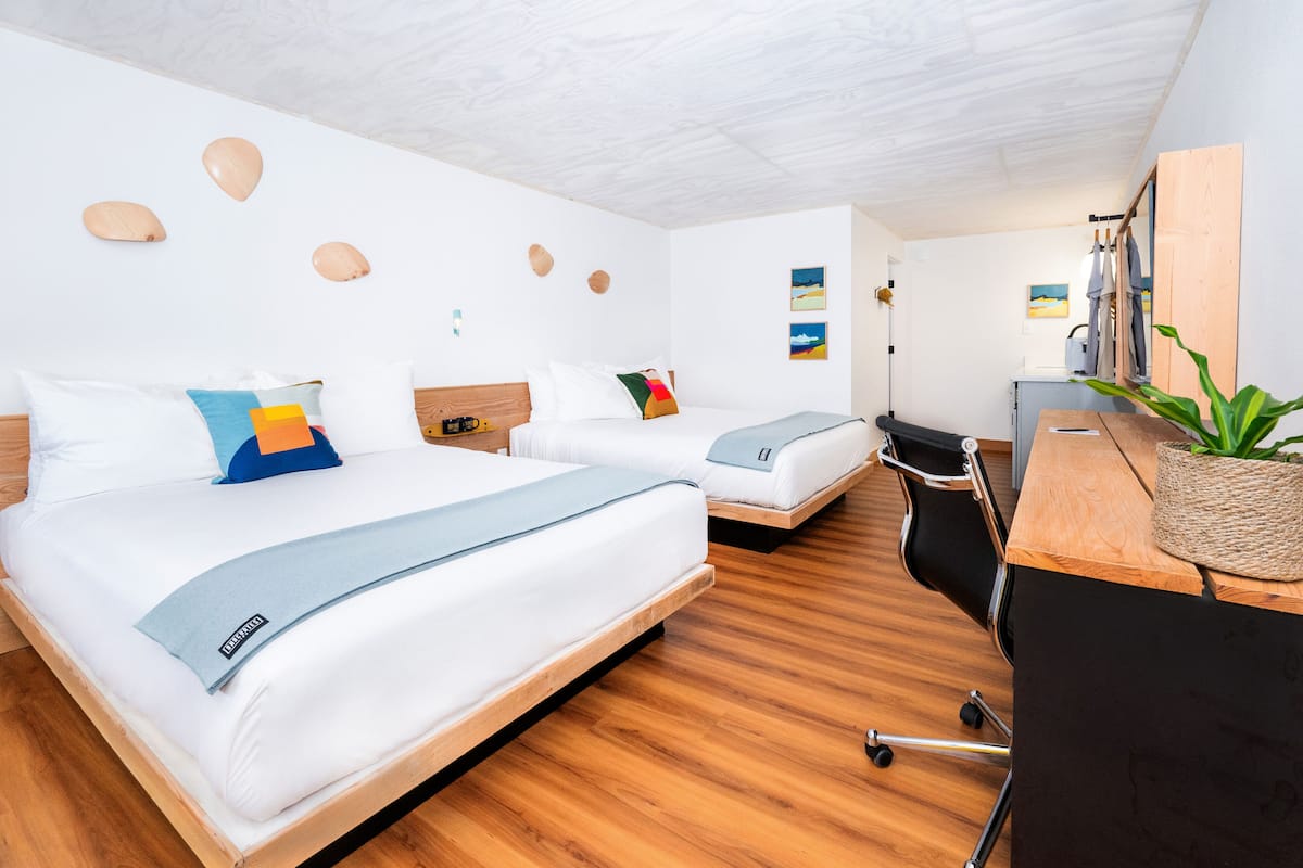 A modern hotel room with two beds, a desk, and a chair.