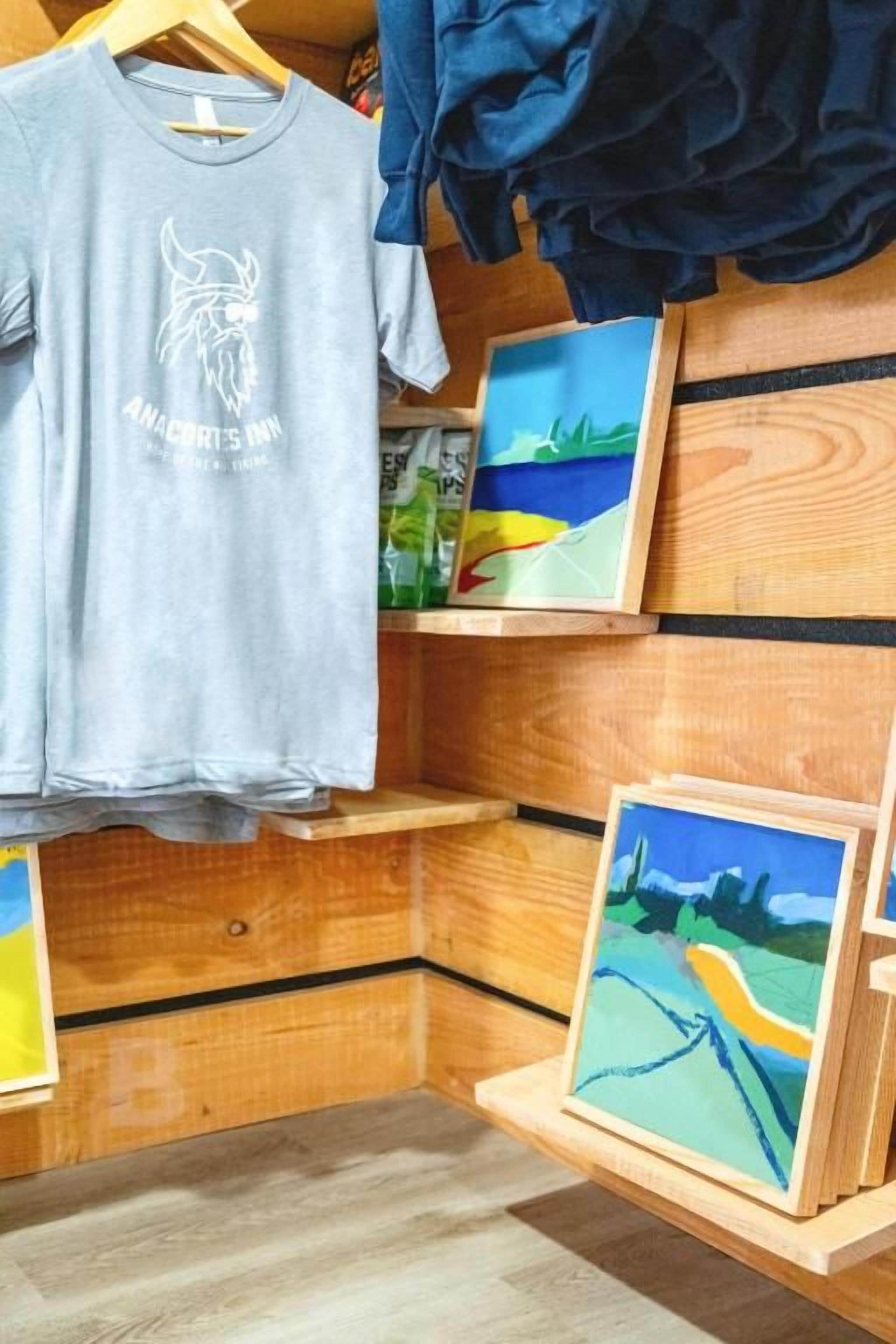 Una habitación con una pared de madera, una camiseta gris colgada en un perchero y dos cuadros en estanterías.