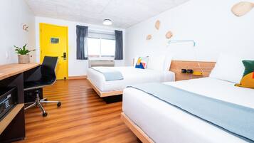A hotel room with a wooden floor, a desk with a chair, two beds, a small table, and a window with curtains.