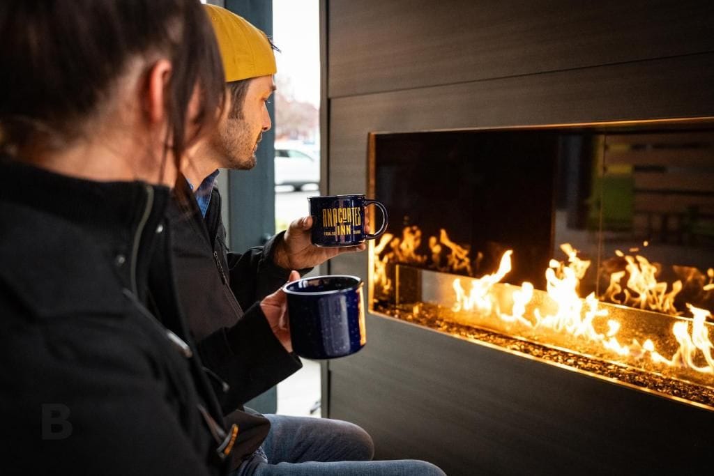 Eine Person hält eine Tasse, im Hintergrund ist ein Kamin zu sehen.