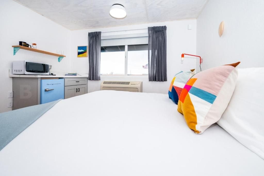 A hotel room with a bed, a desk with a microwave, a small kitchenette, and a window with curtains.