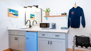 A modern kitchen with a white countertop, a blue dishwasher, a microwave, and a hanging blue hoodie.