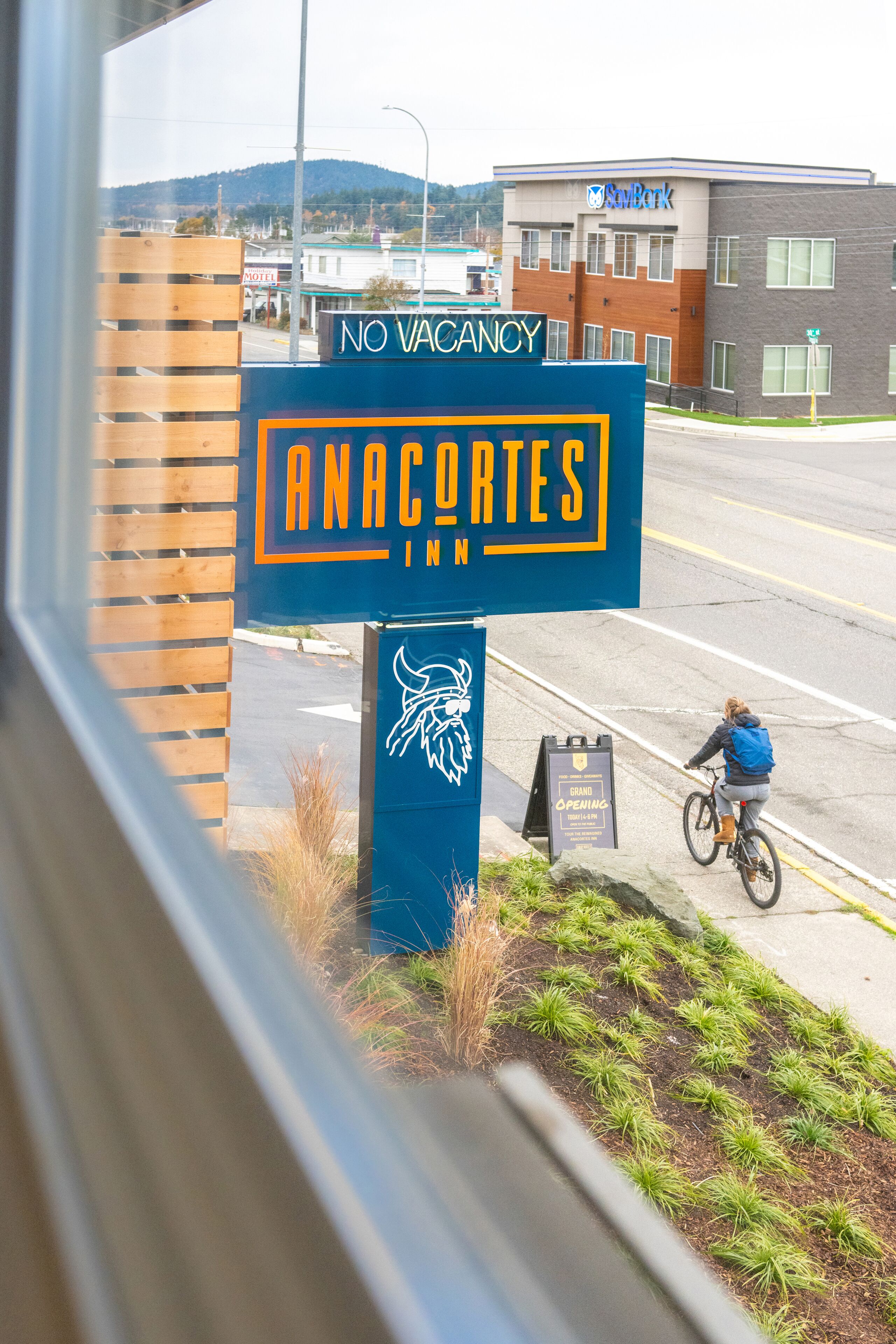 Placa para 'Anacortes Inn' com aviso de 'SEM QUARTOS DISPONÍVEIS', logotipo Viking e placa de 'GRANDE ABERTURA' na calçada.