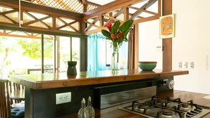 A kitchen with a wooden countertop, a gas stove, a vase with flowers, and a window with blue curtains. - Kenaki Lodge (Cahuita)