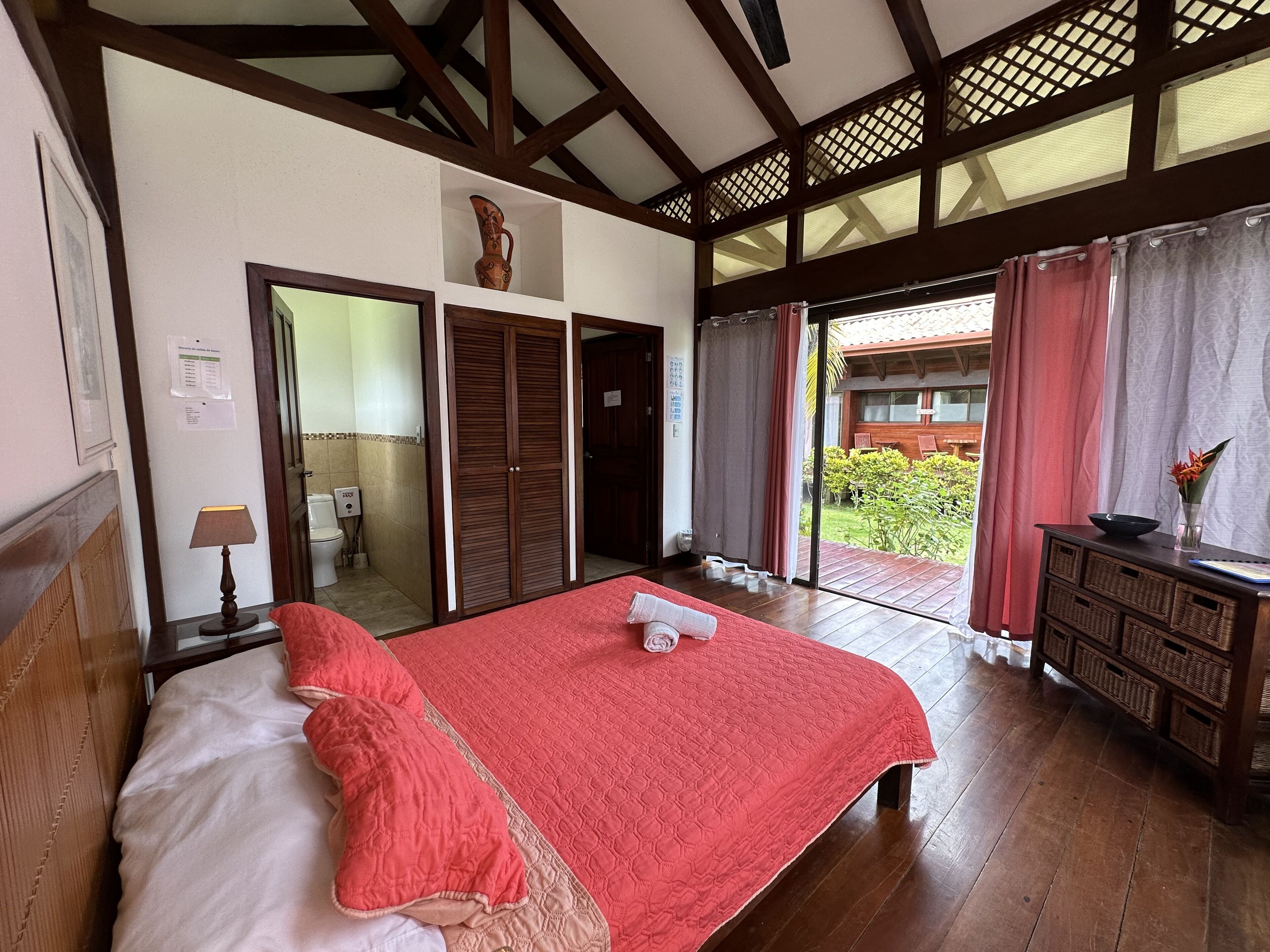 A bedroom with a large bed, wooden wardrobe, and a view of the garden through a sliding door.