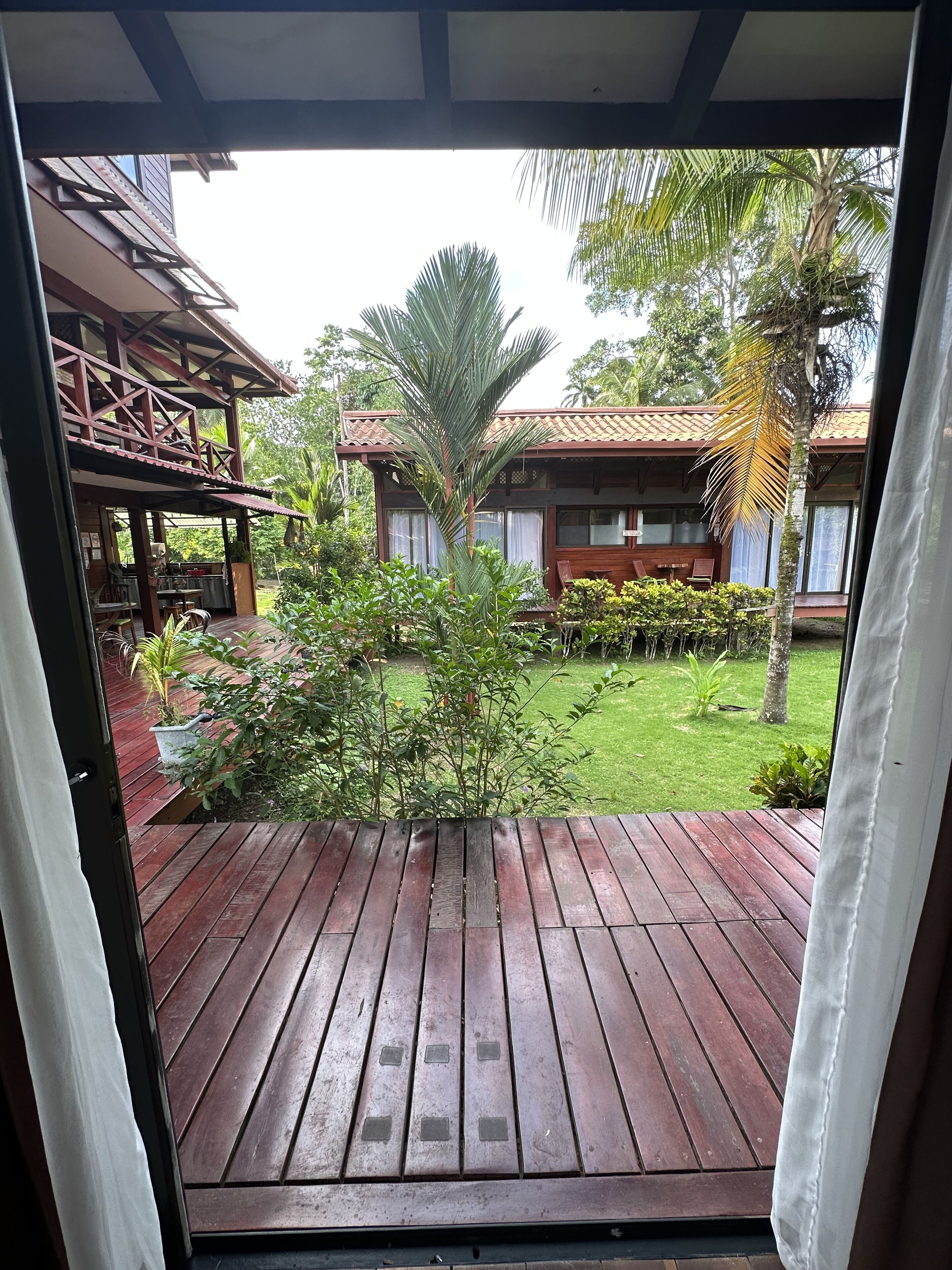 Une terrasse en bois offrant une vue sur un bâtiment doté d’un toit en tuiles et d’un espace extérieur aménagé avec des sièges.