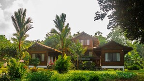 A two-story wooden house with a balcony, surrounded by lush greenery and palm trees. - Kenaki Lodge (Cahuita)