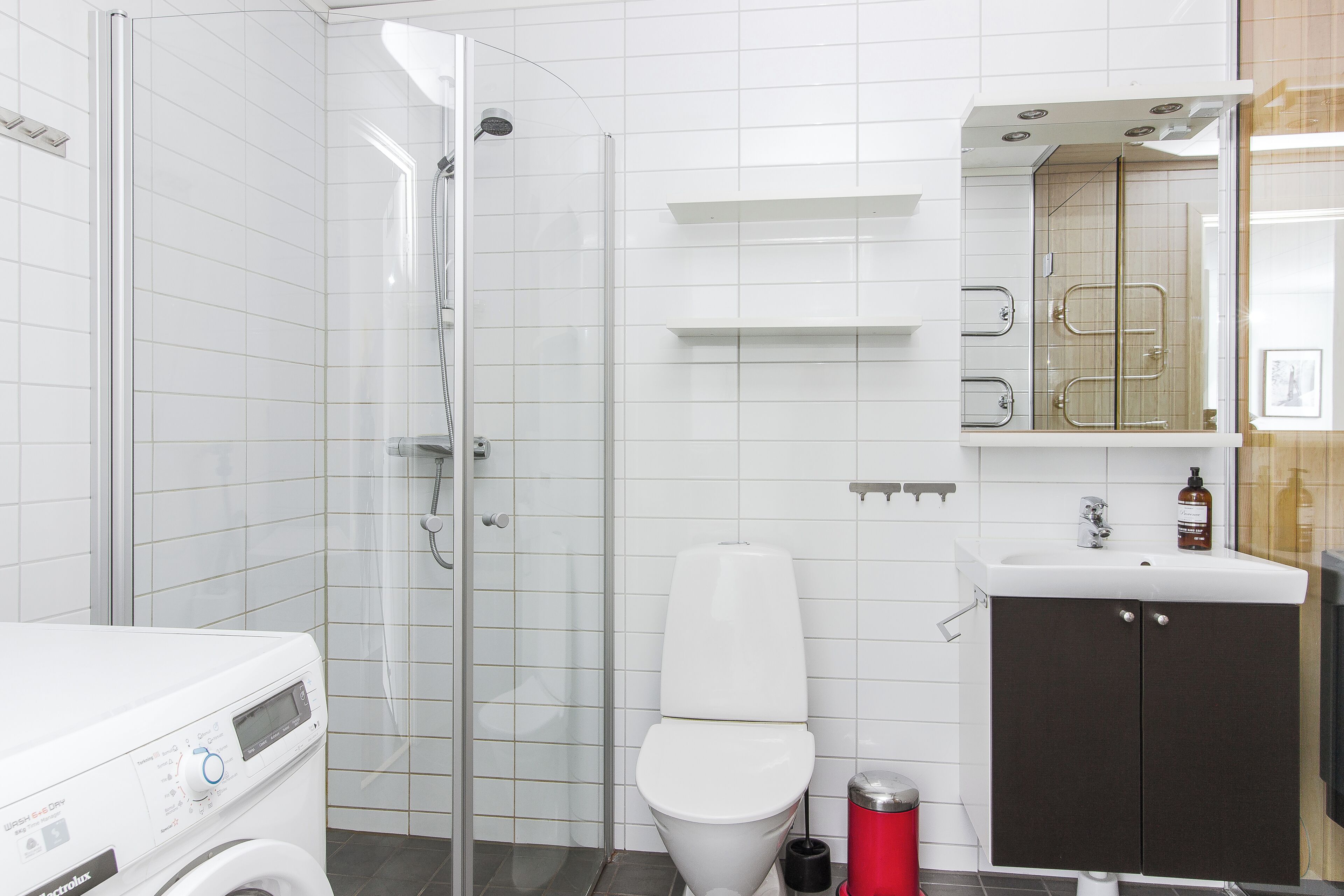 A modern bathroom with a glass shower enclosure, a white toilet, a sink with a mirror, and a washing machine.
