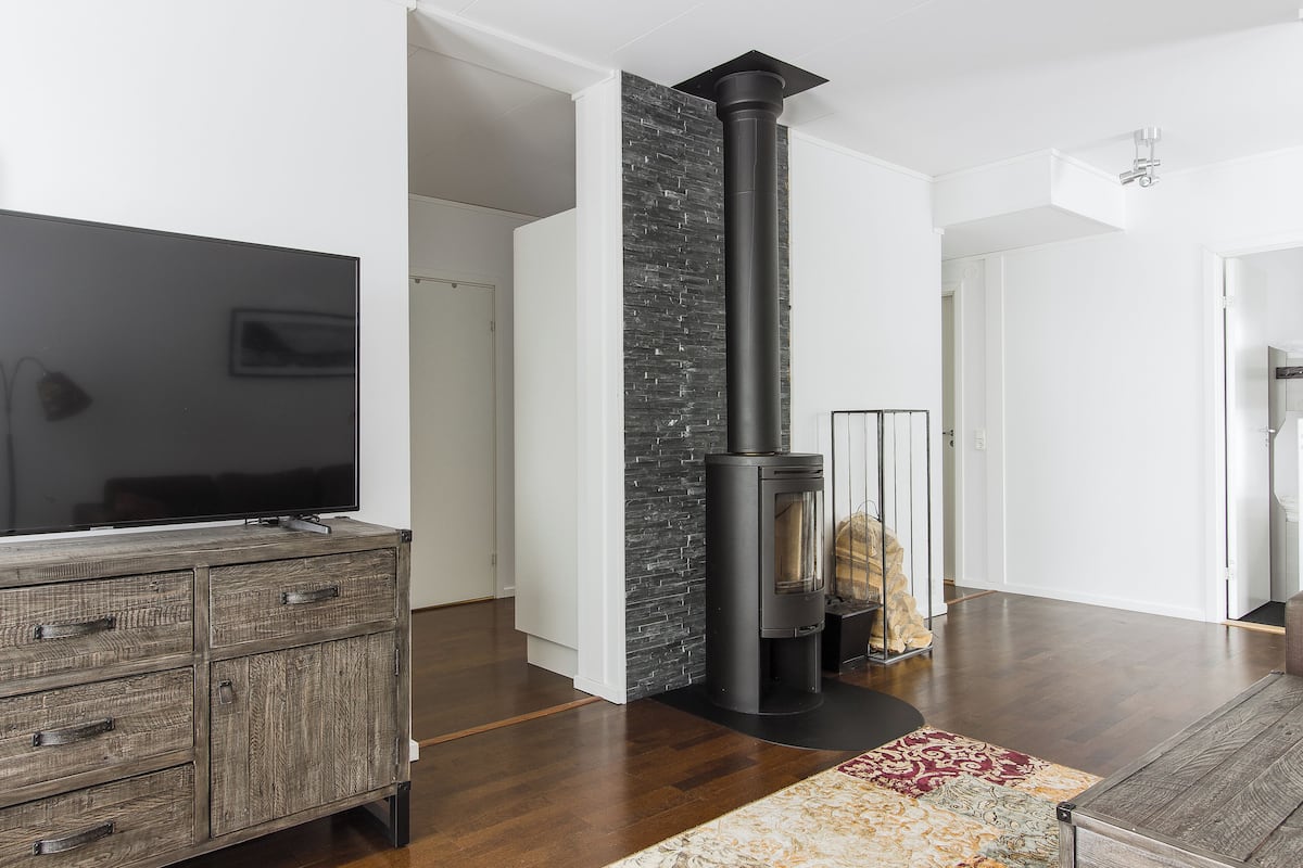 Ein modernes Wohnzimmer mit einem großen Flachbildfernseher, einem Holzkabinett, einem schwarzen Kamin und einem gemusterten Teppich.
