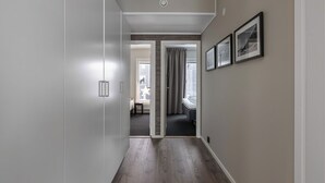 Un pasillo con piso de madera, una puerta que da a una habitación con cama y cortinas, y cuadros enmarcados en la pared.