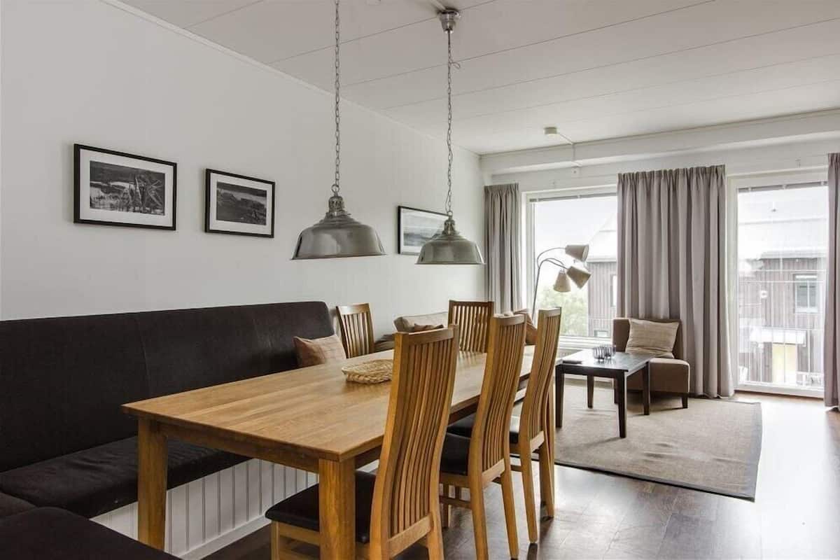 Ein modernes Wohnzimmer mit Esstisch aus Holz, einer schwarzen Ledersofa und Blick auf die Stadt durch große Fenster.