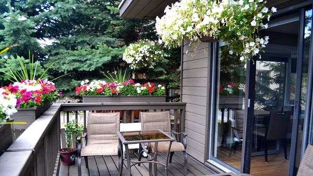 A wooden deck with outdoor furniture, potted plants, and hanging flower baskets. - A Good Nite's Rest Bed and Breakfast (Banff)