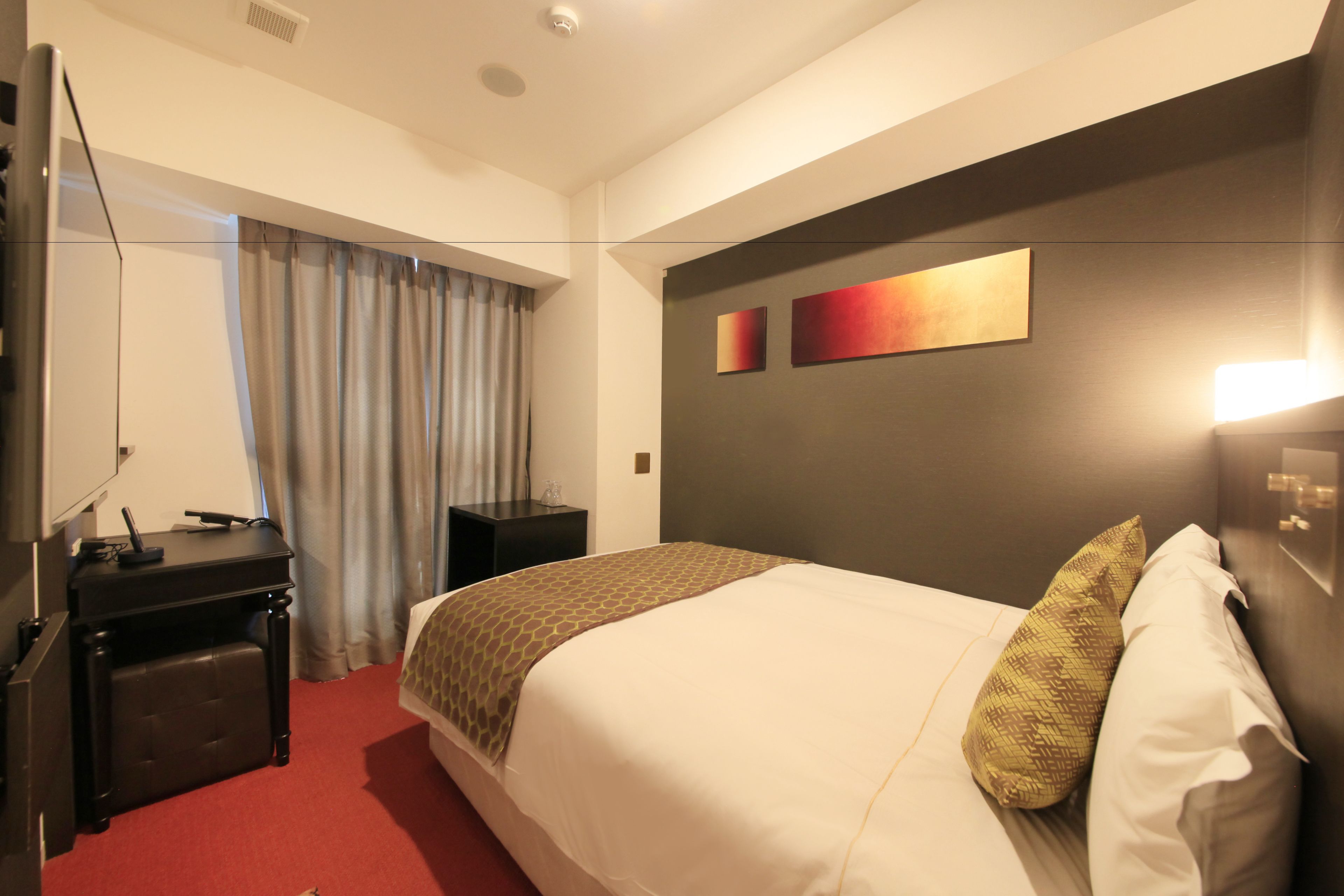 A hotel room with a bed, a desk, a chair, a TV, and a window with curtains.