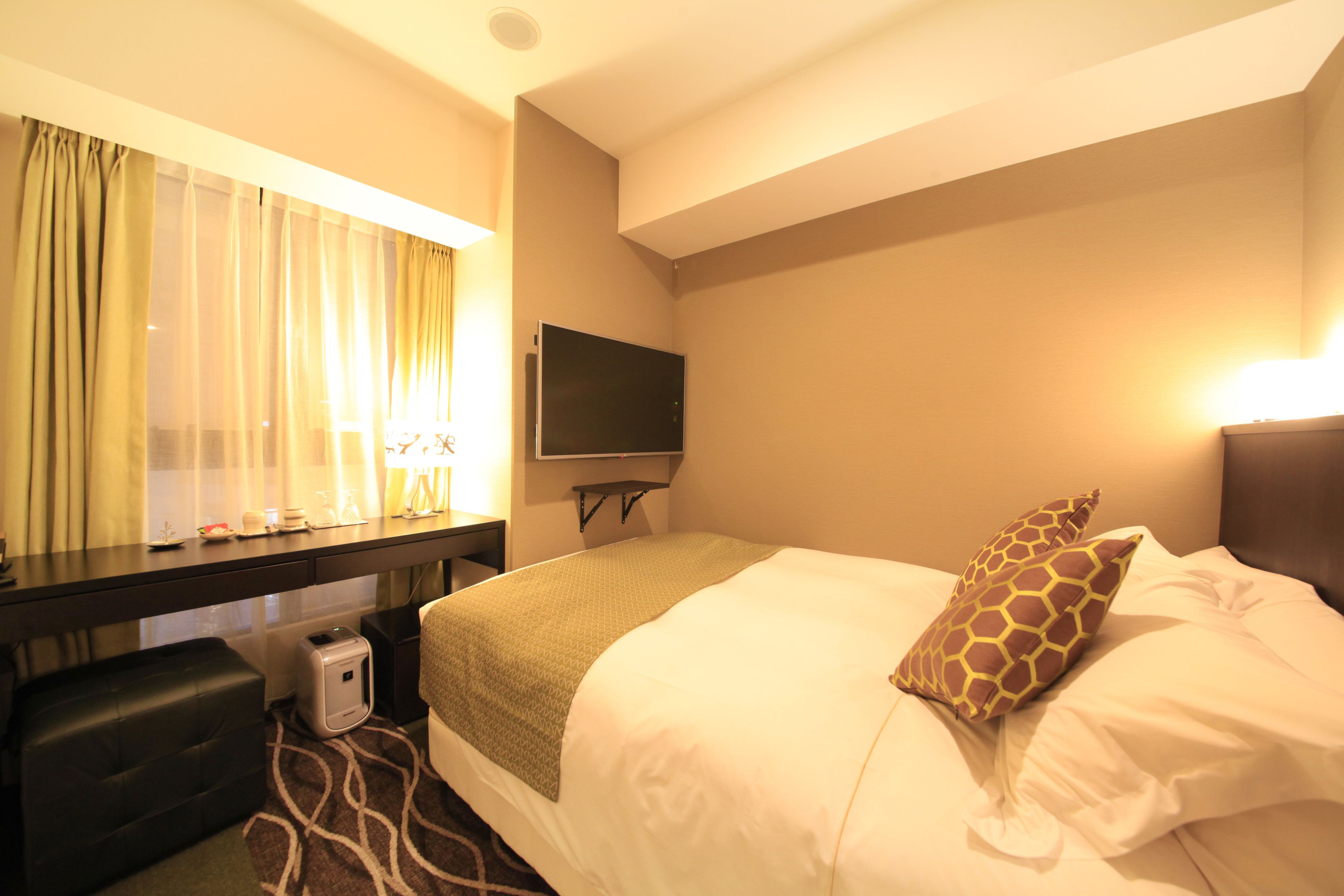 A hotel room with a bed, a desk, a television, and a window with curtains.