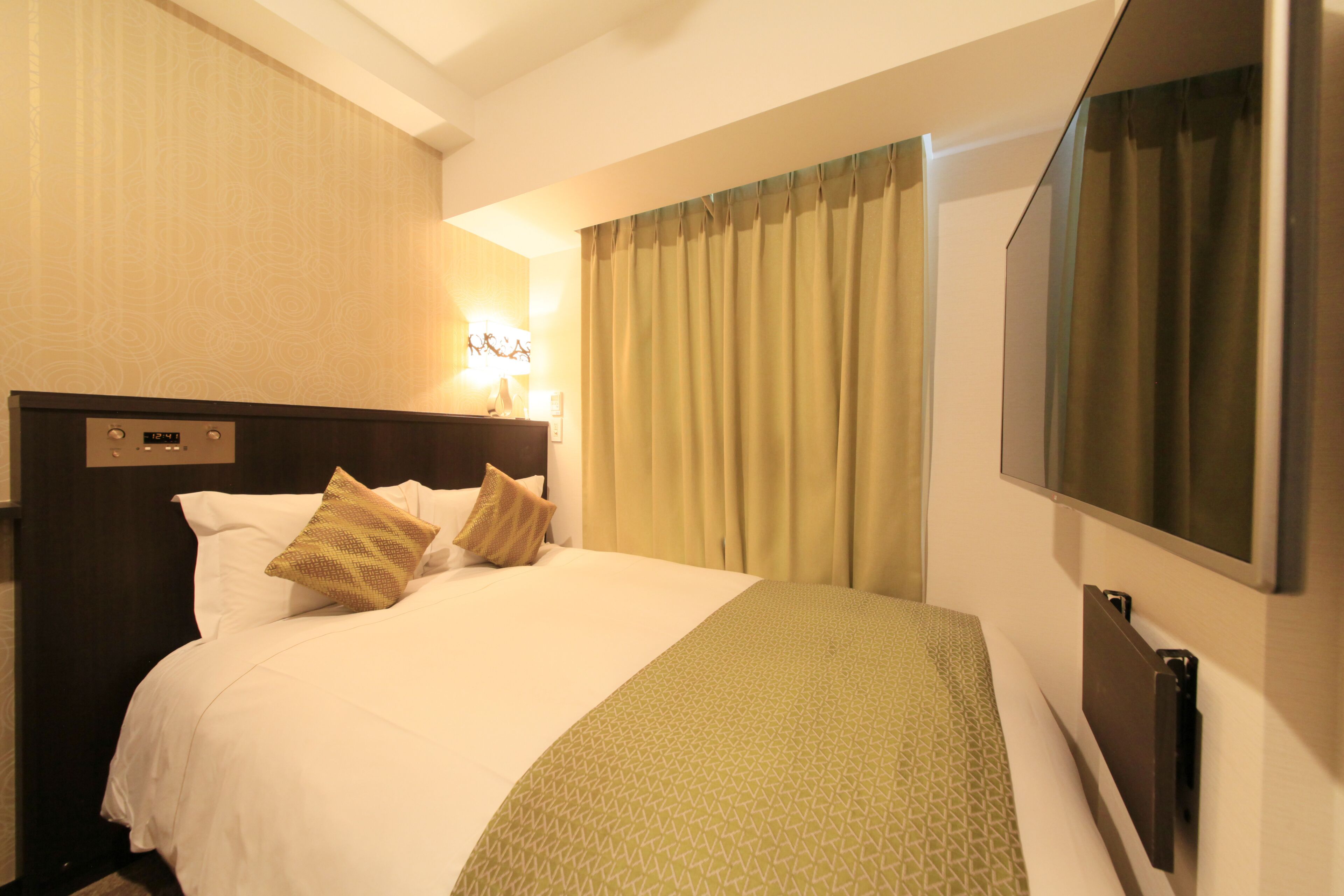 A hotel room with a large bed, a TV mounted on the wall, and a window with curtains.