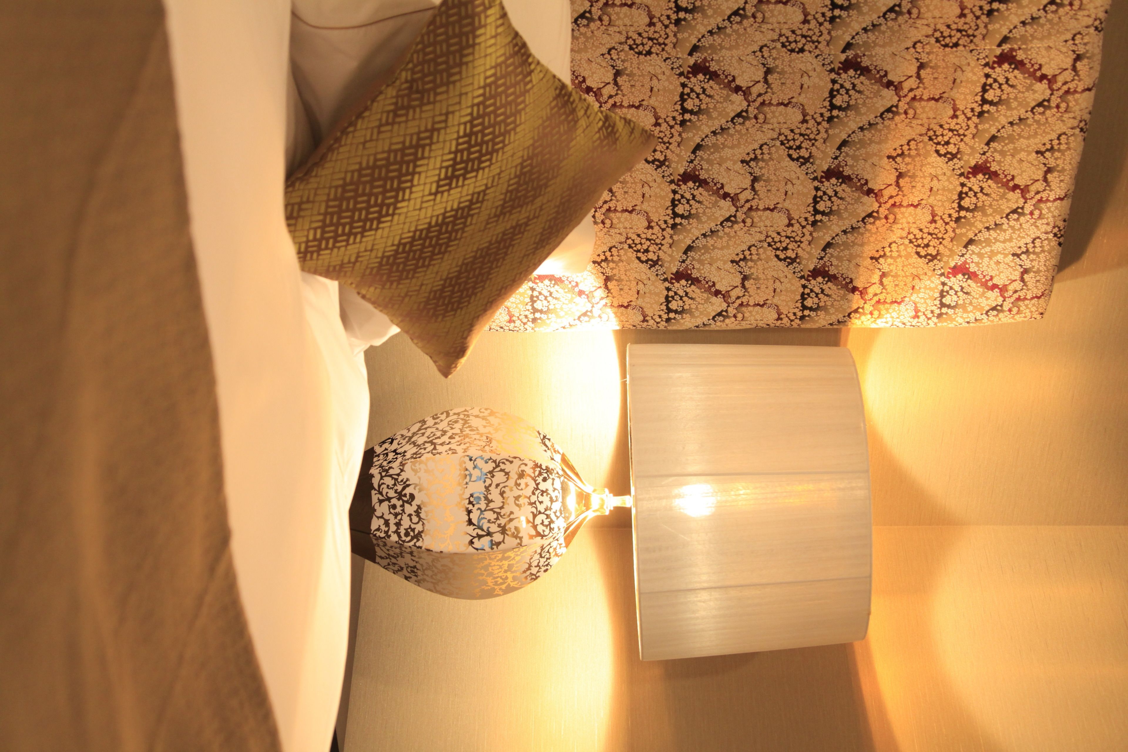 Ein Zimmer mit einem gemusterten Wandhintergrund, einer weißen Lampe und einem grünen Kissen.