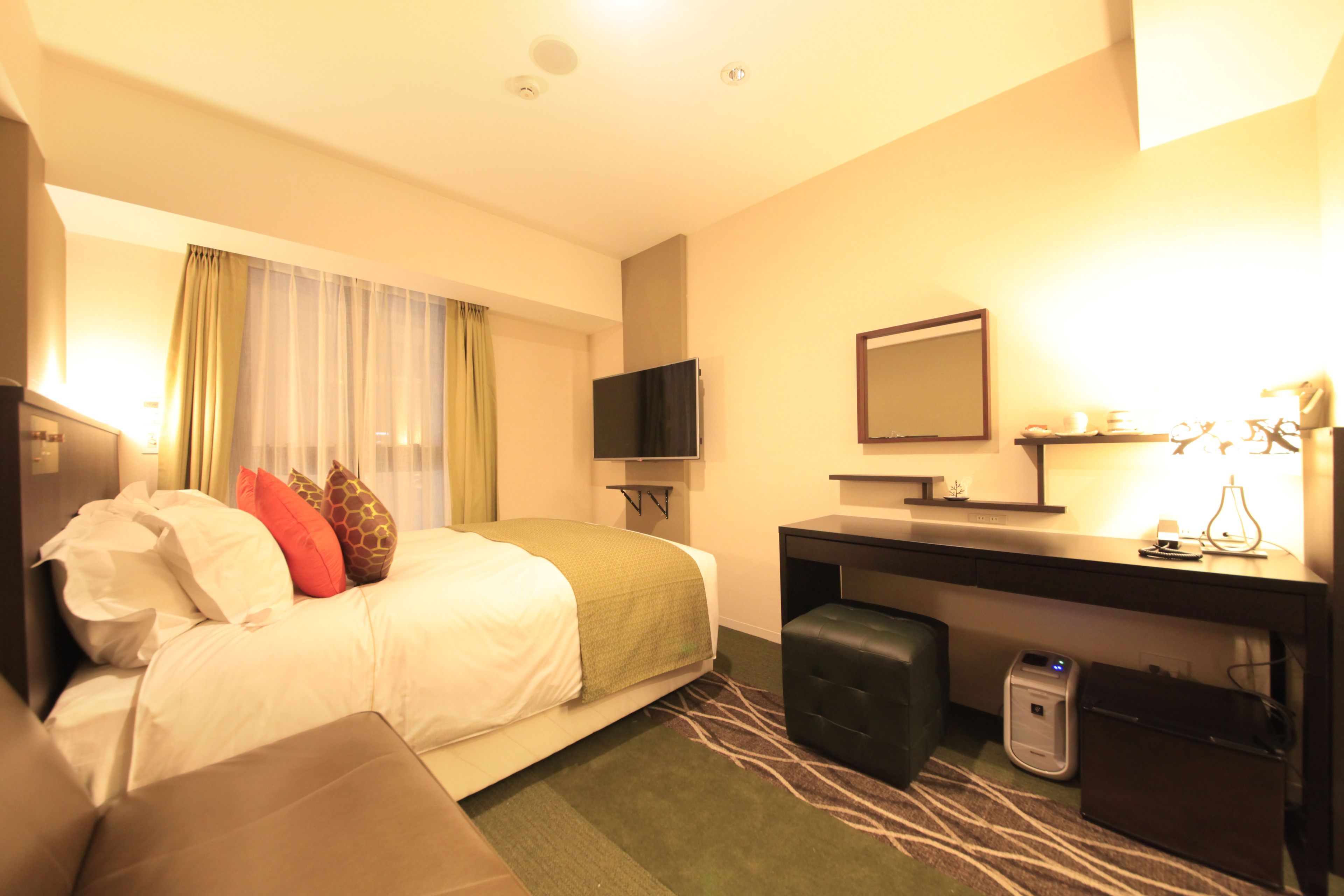 A hotel room with a bed, a desk, a television, a mirror, and a suitcase.