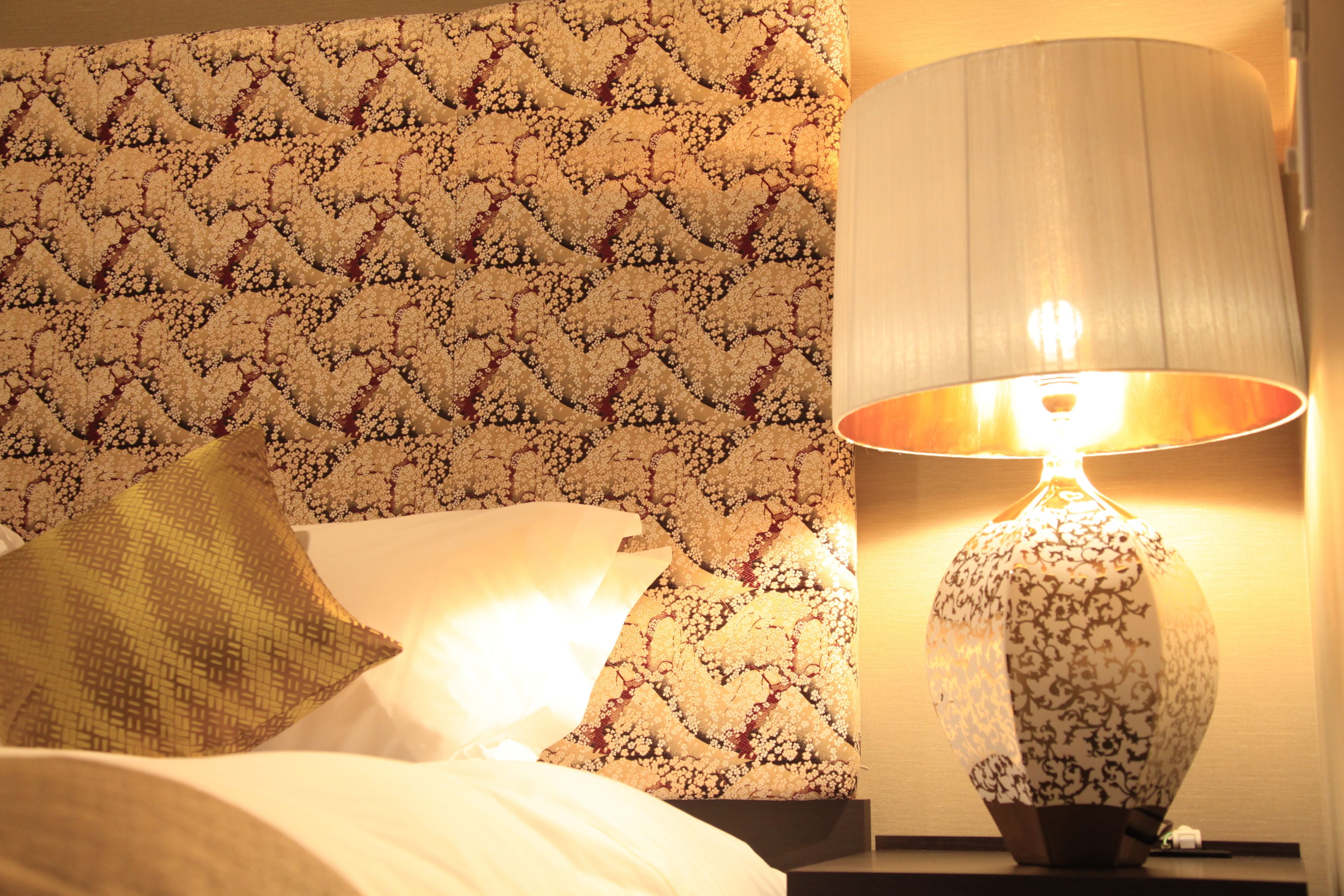 A bed with a patterned headboard, a bedside lamp, and a pillow.