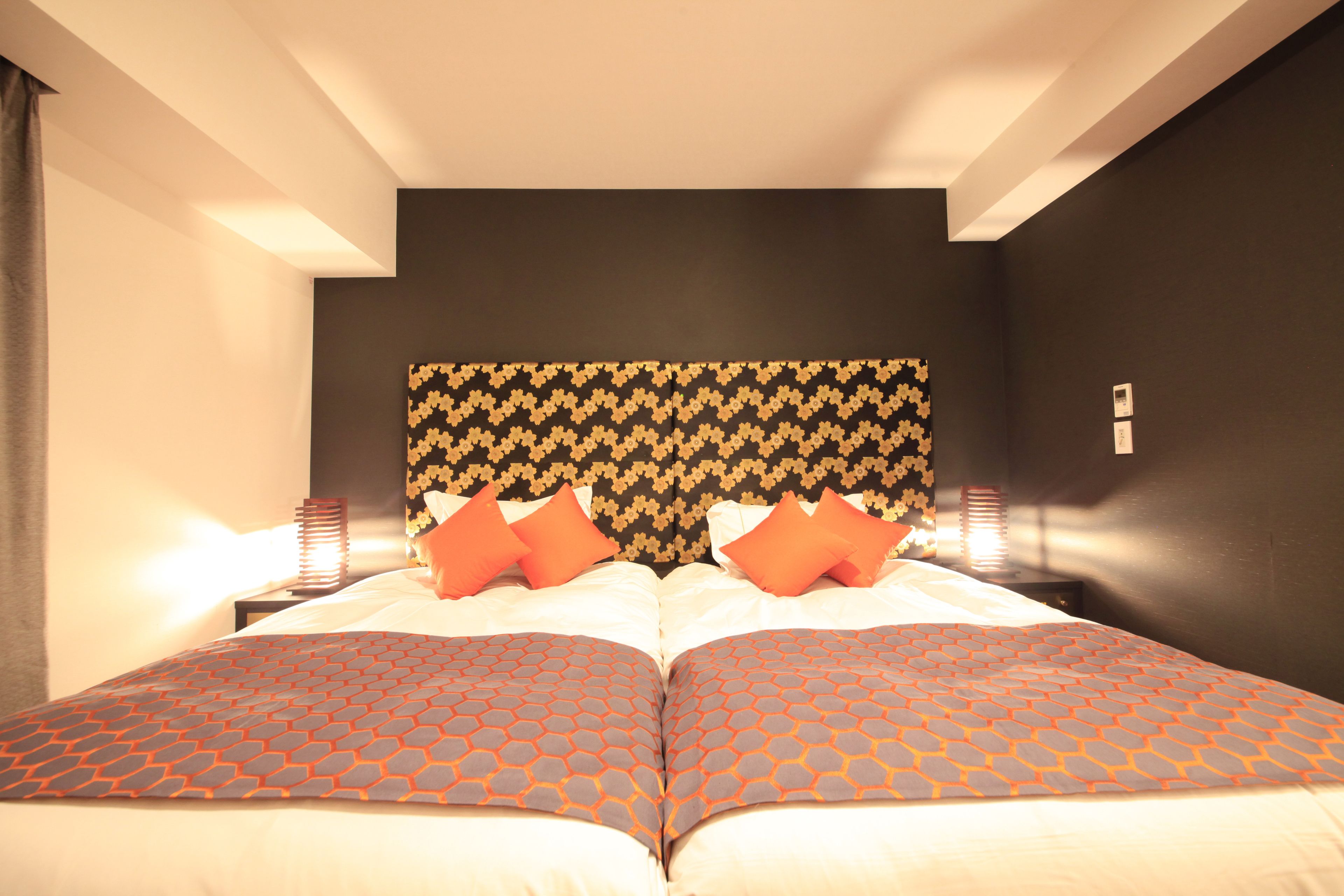 Un lit double avec une tête de lit à motifs, deux tables de chevet avec des lampes et un mur de couleur sombre.