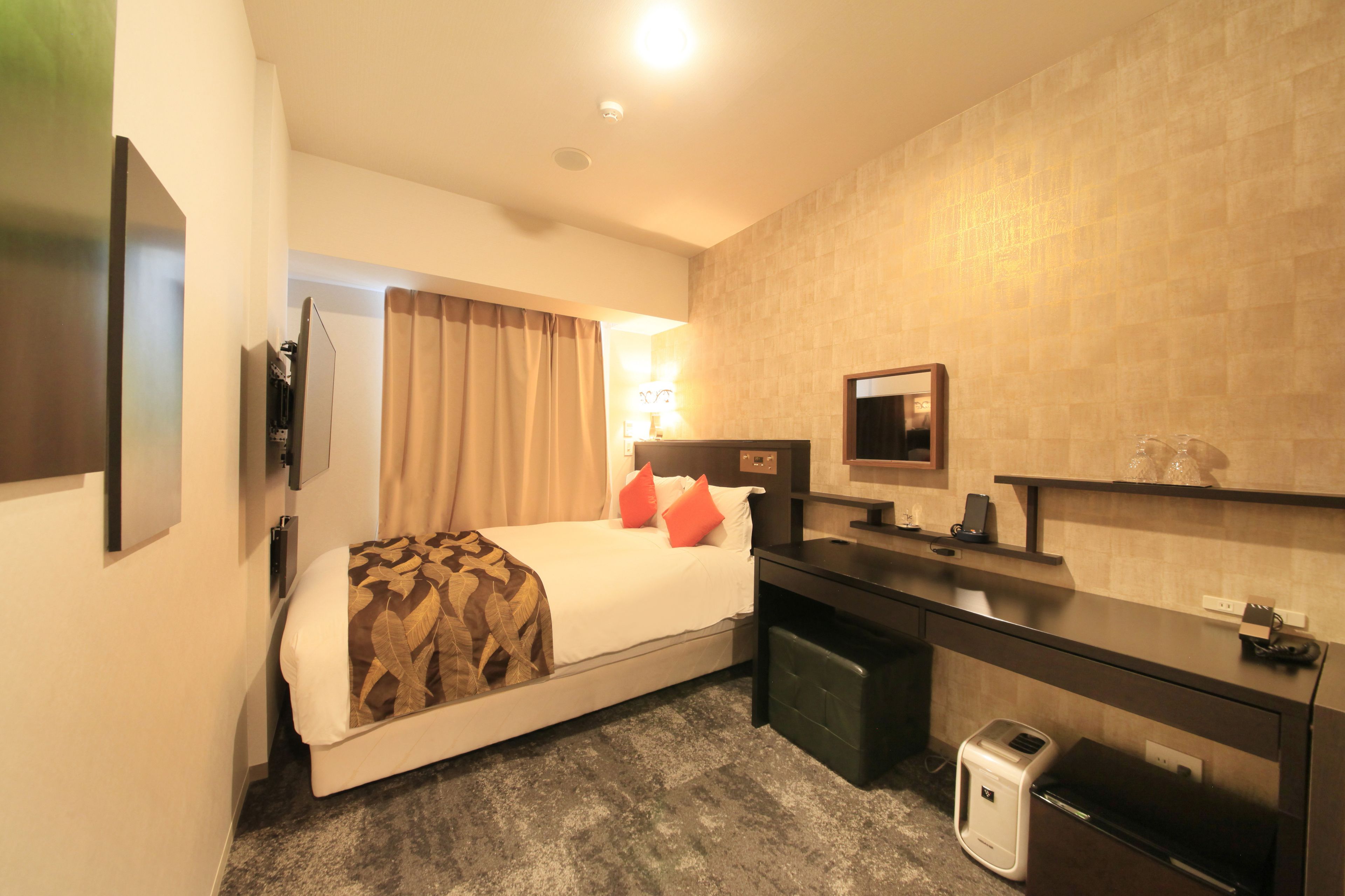 A hotel room with a bed, bedside table, TV, and a small desk with a chair.