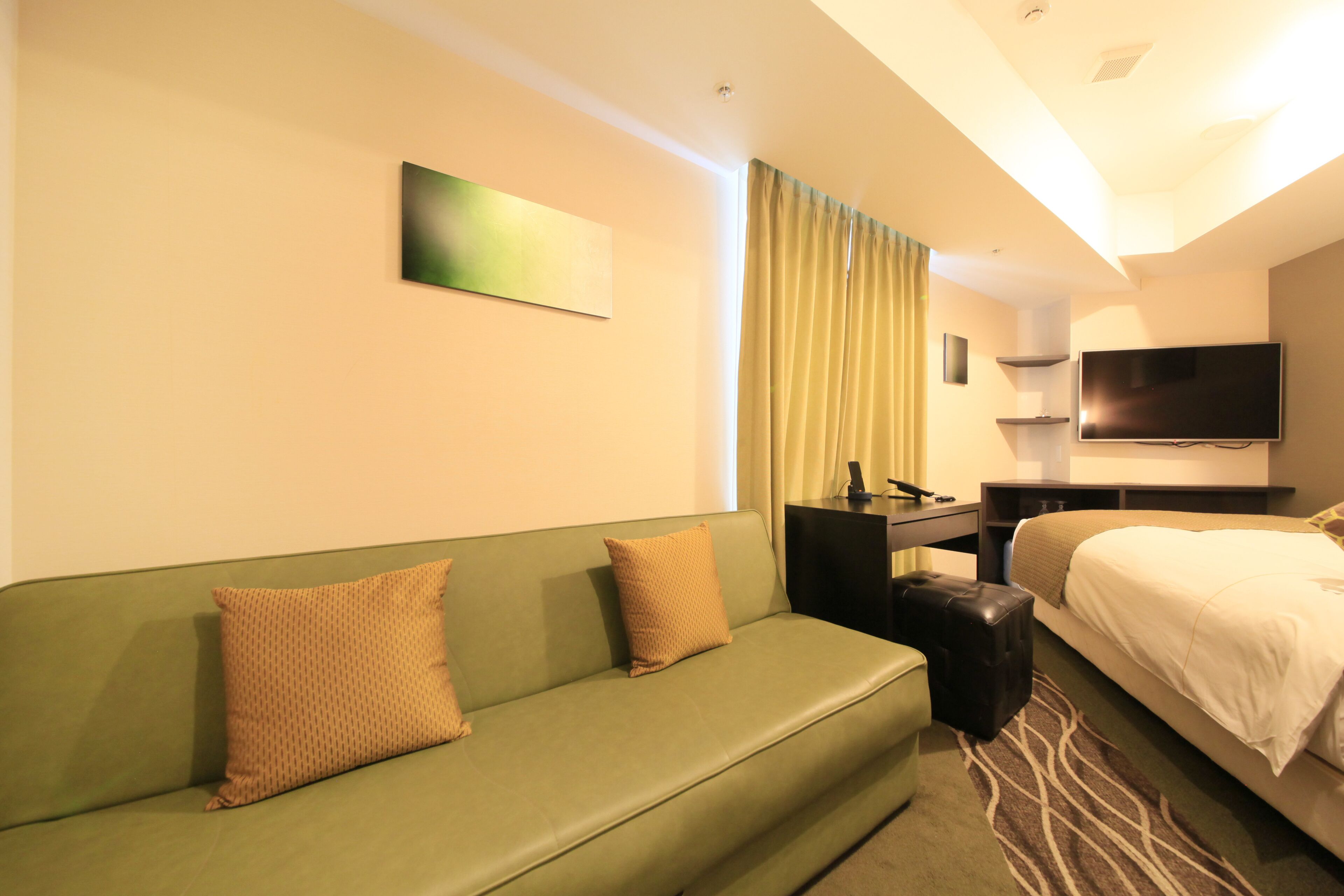 A hotel room with a green sofa, a bed, a flat-screen TV, and a small table.