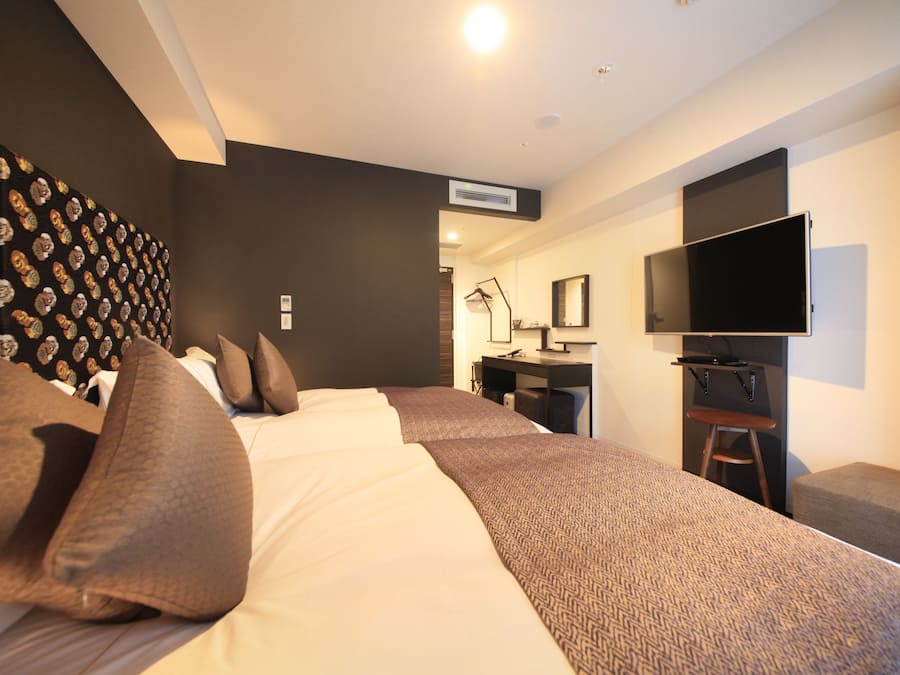 A modern hotel room with a large bed, a desk, a flat-screen TV, and a patterned wall.