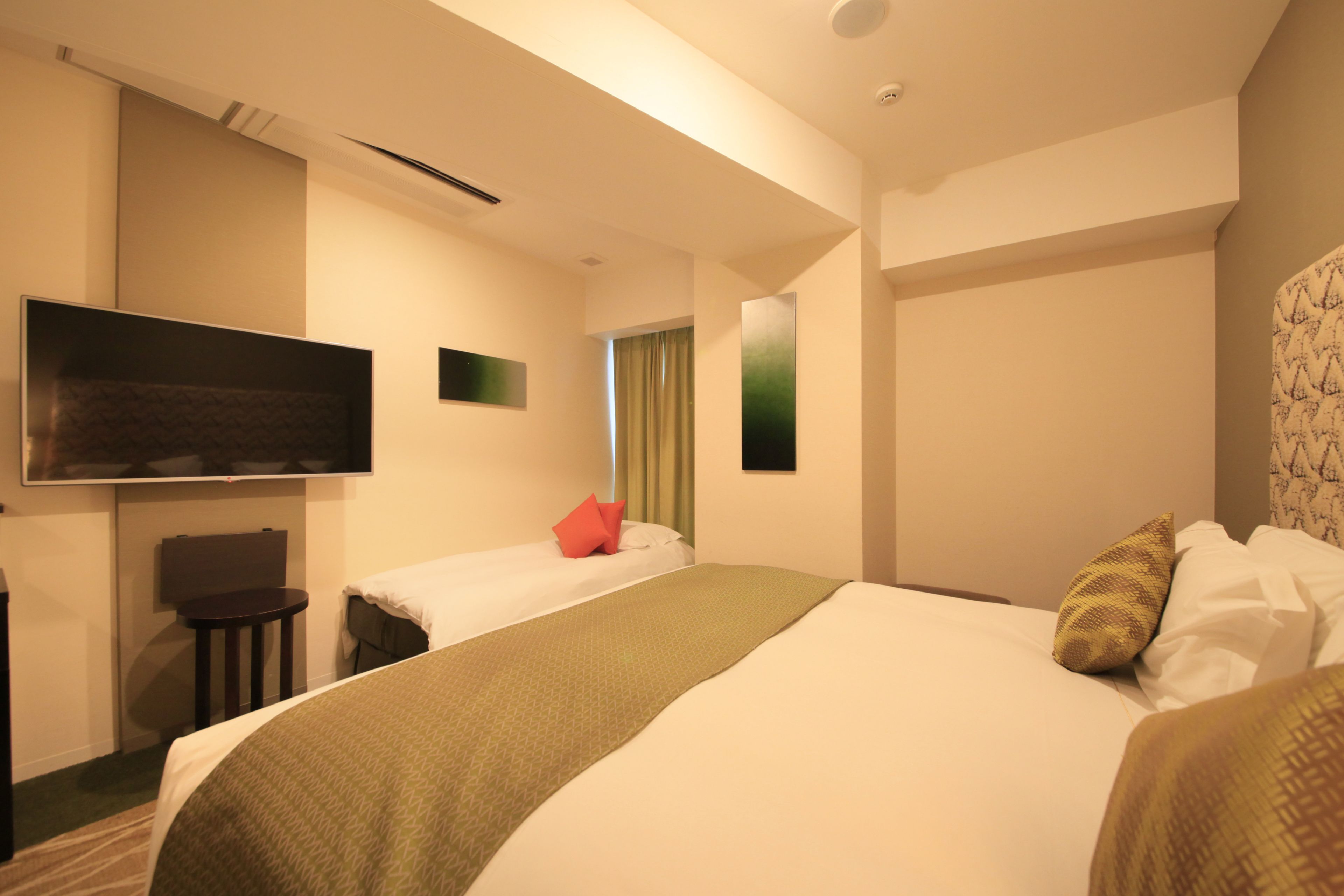 Habitación de hotel con una cama grande, una cama más pequeña, un televisor de pantalla plana en la pared, un escritorio con una silla y una ventana con cortinas.