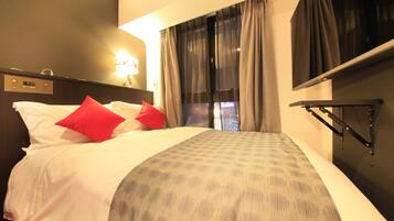 A hotel room with a bed, a nightstand, a wall clock, and a window with curtains.