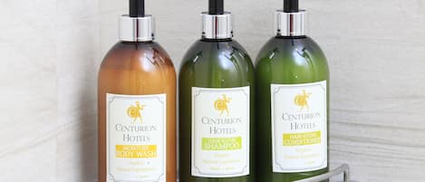Tres botellas de productos para el cabello de Centurion Hotels sobre un estante transparente.