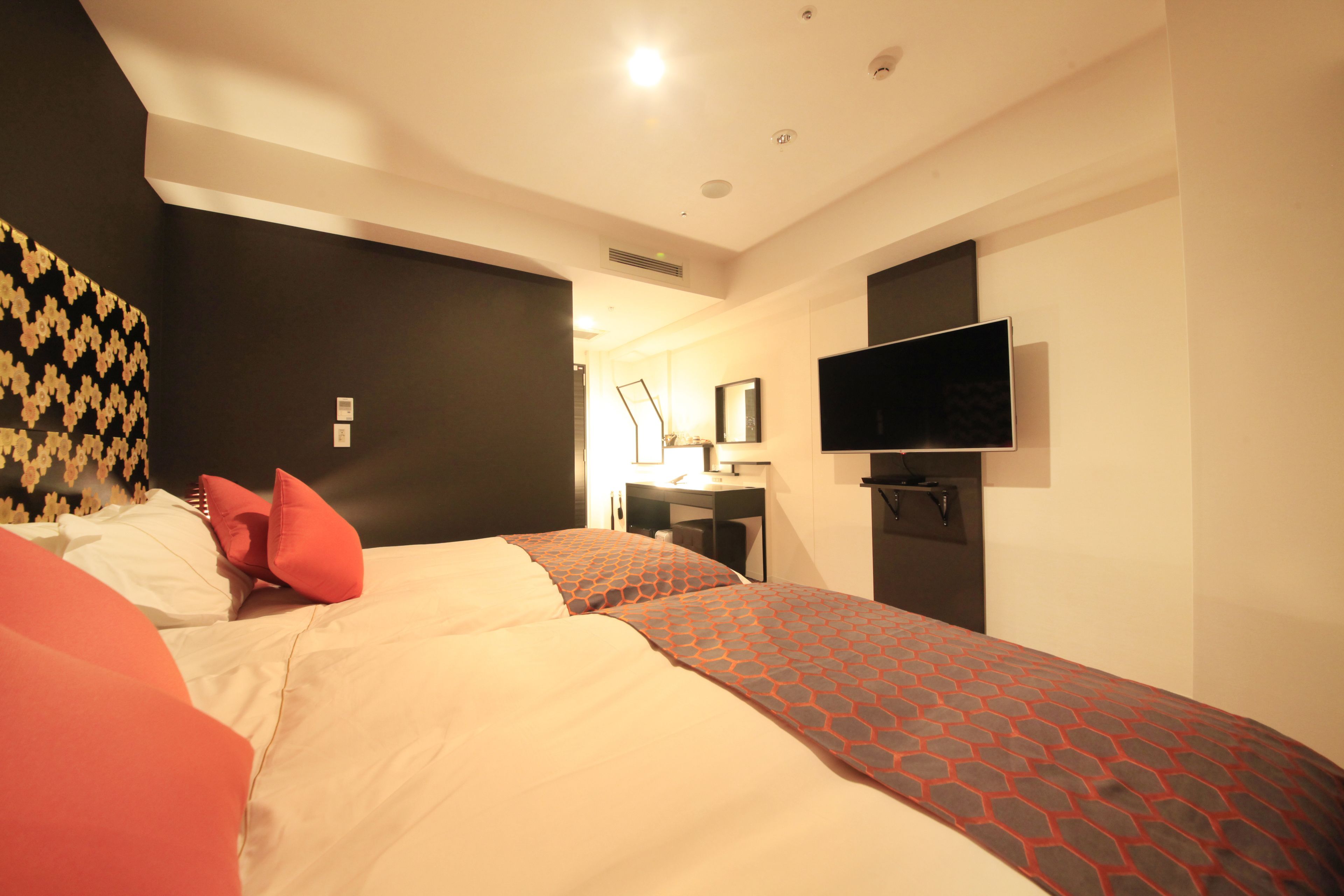 A hotel room with two beds, a TV mounted on the wall, a desk with a chair, and a mirror.